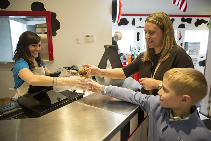 A woman serves a mother and a child with an ice cream cone.