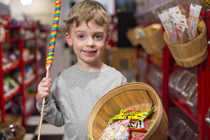 A boy holding a cany stick and a bucket with various candy products